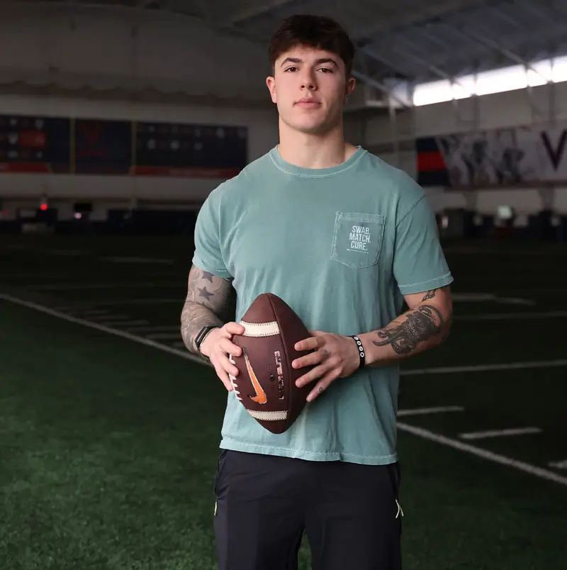 Robbie Engelberg holding a football in the University of Virginia indoor practice facility