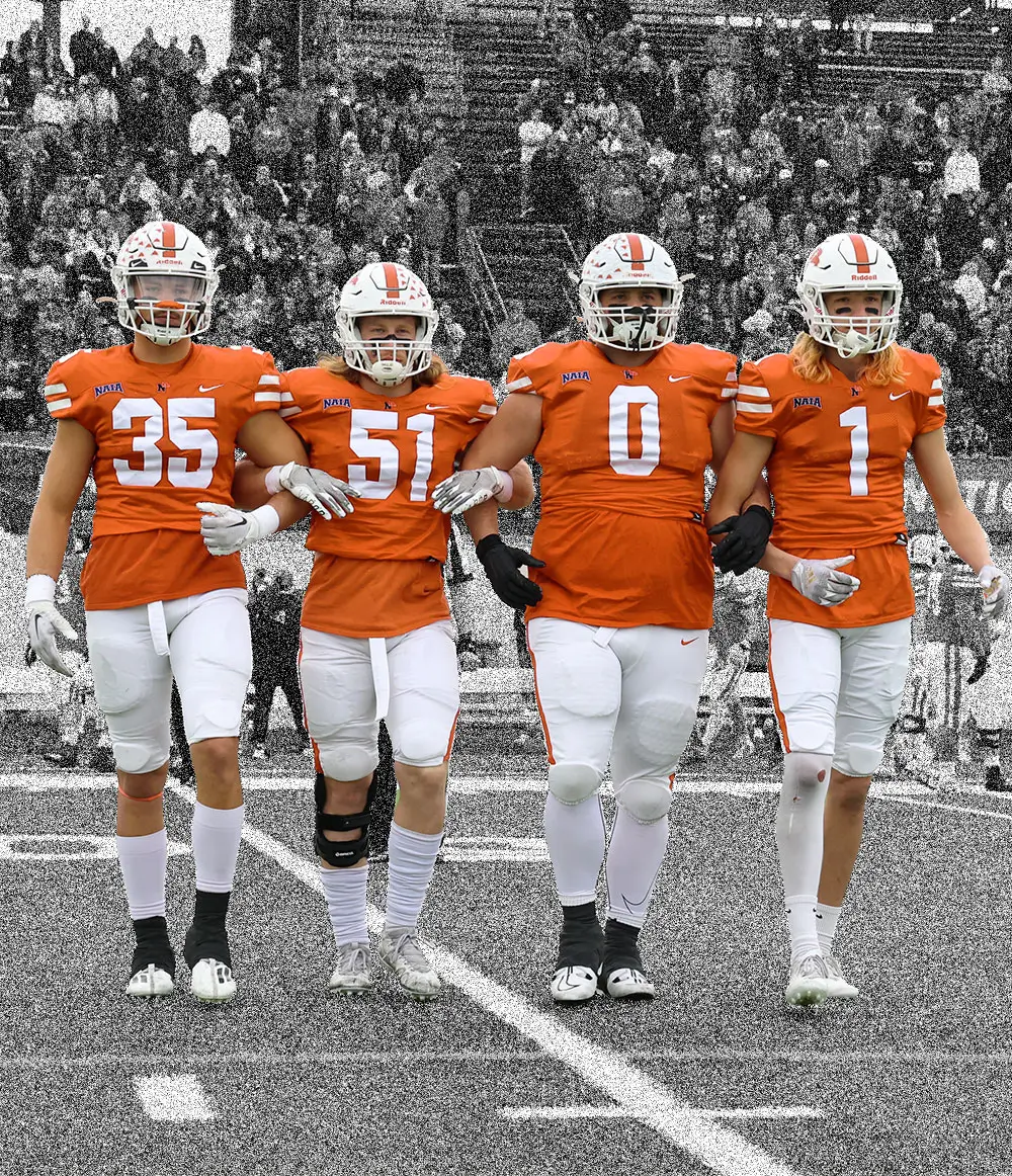 Four college football players walking onto the field