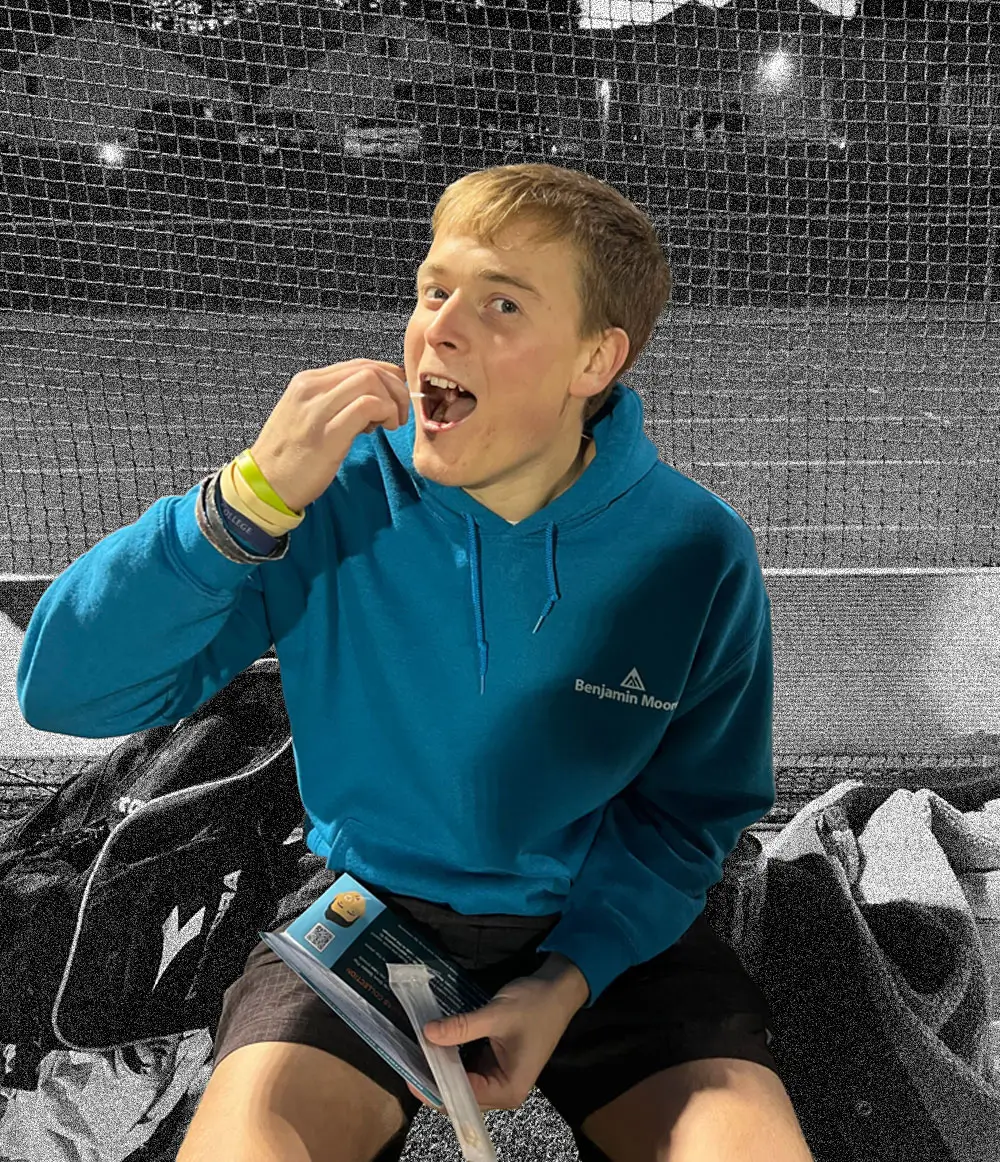 A student athlete swabbing his cheek on the sideline